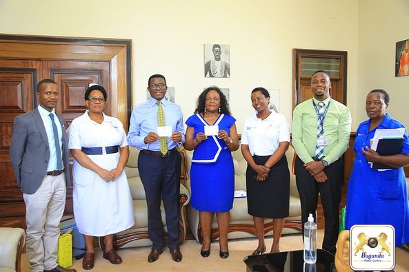 The Katikkiro and his wife (in the middle) are pictured holding their vaccination cards, with a team of medical personnel Image