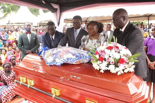 Katikkiro laying a wreath on the coffin with the wife and his deputies. Image